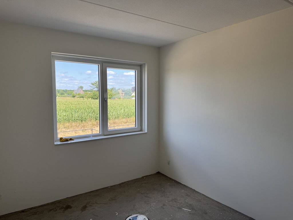 Lege nieuwe slaapkamer met gladde lichte wanden en een raam dat uitkijkt op een maisveld